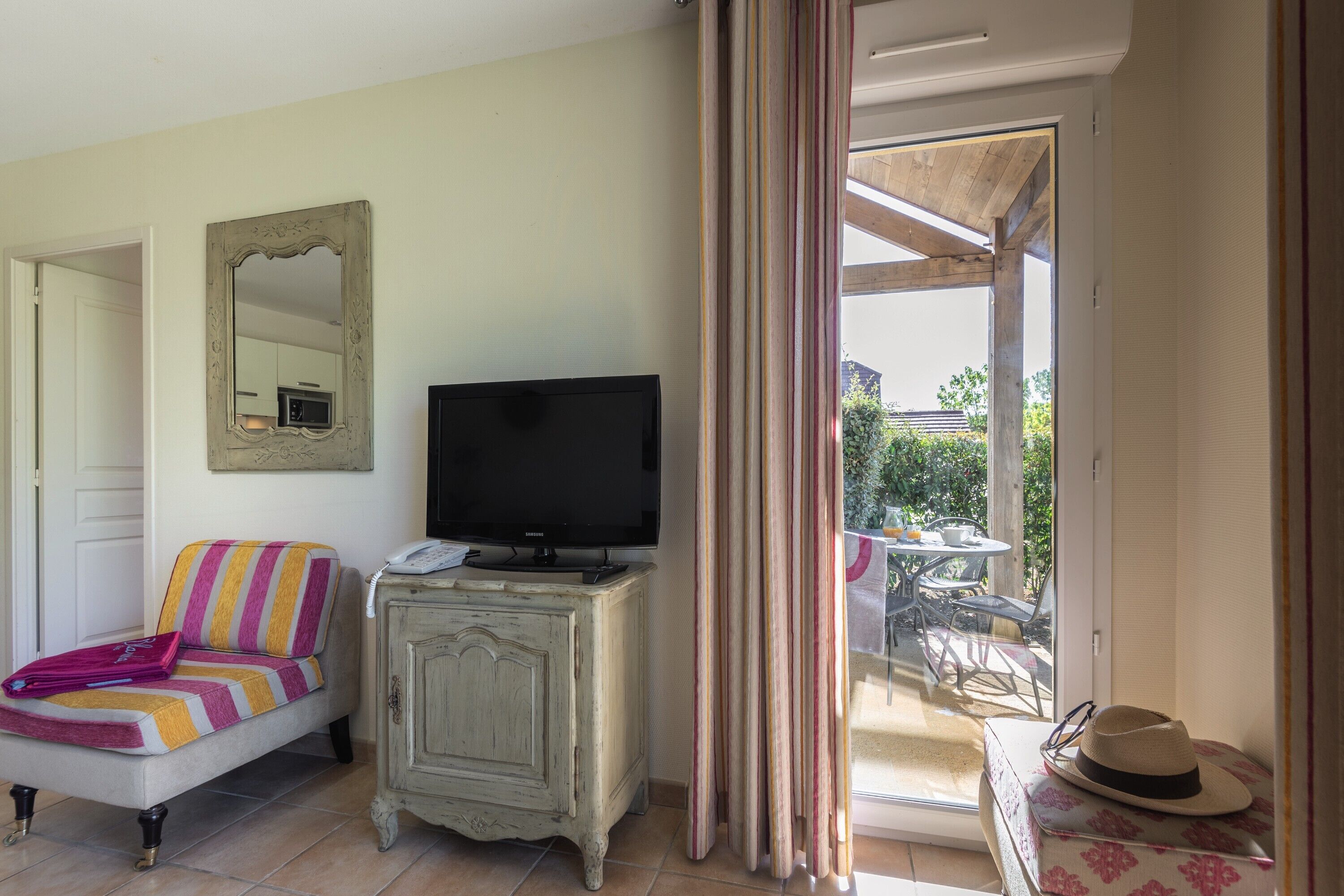 Una habitación con televisión sobre un mueble, un sofá a rayas, un espejo en la pared y vistas del patio exterior.