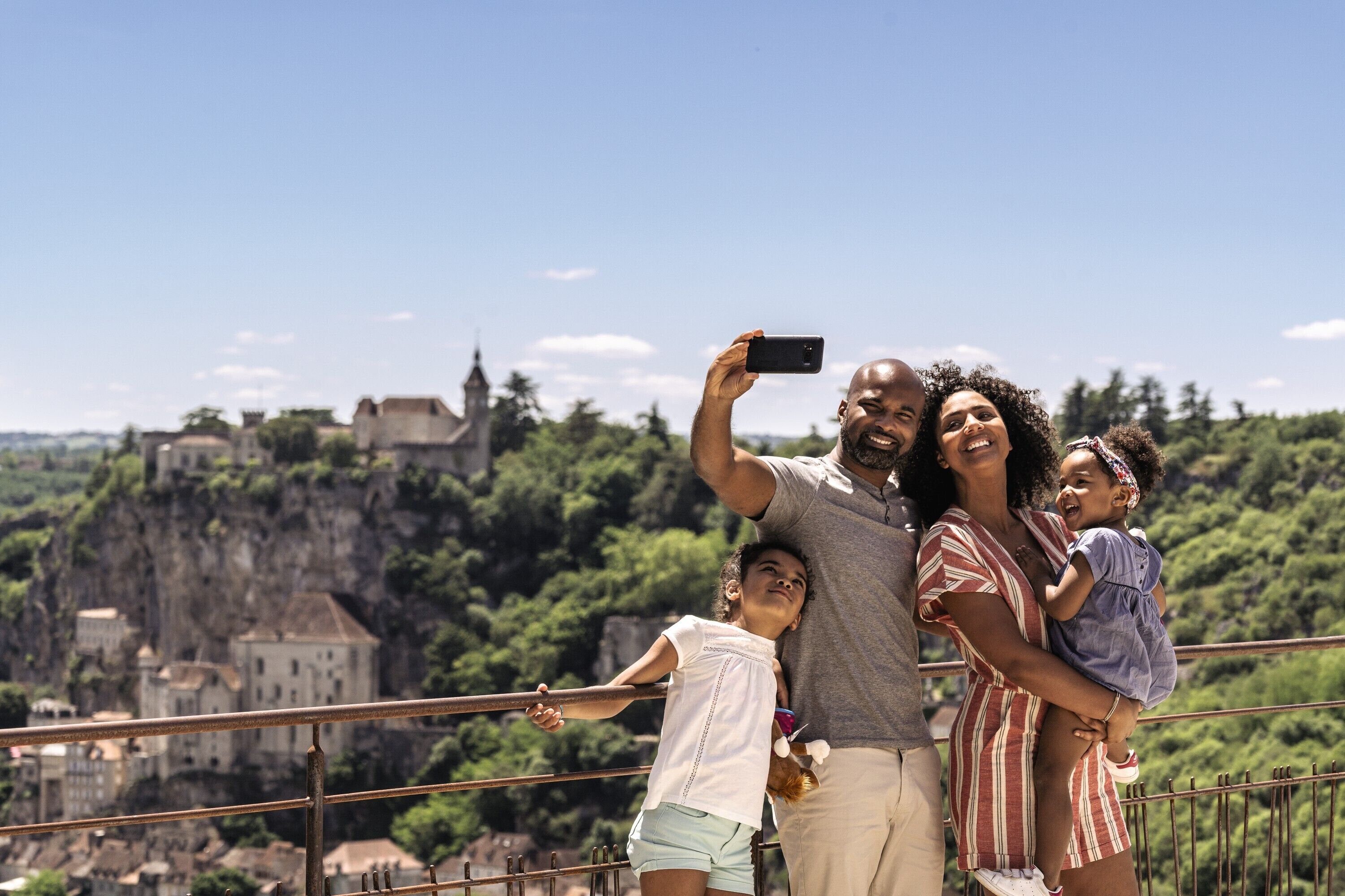 A family taking a selfie on a balcony overlooking a historic town with a castle on a cliff.