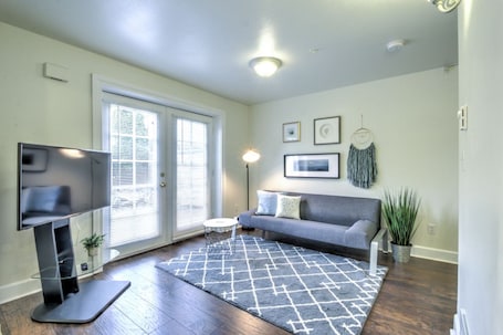 A modern living room with a flat-screen TV, a gray sofa, a patterned rug, and a potted plant.