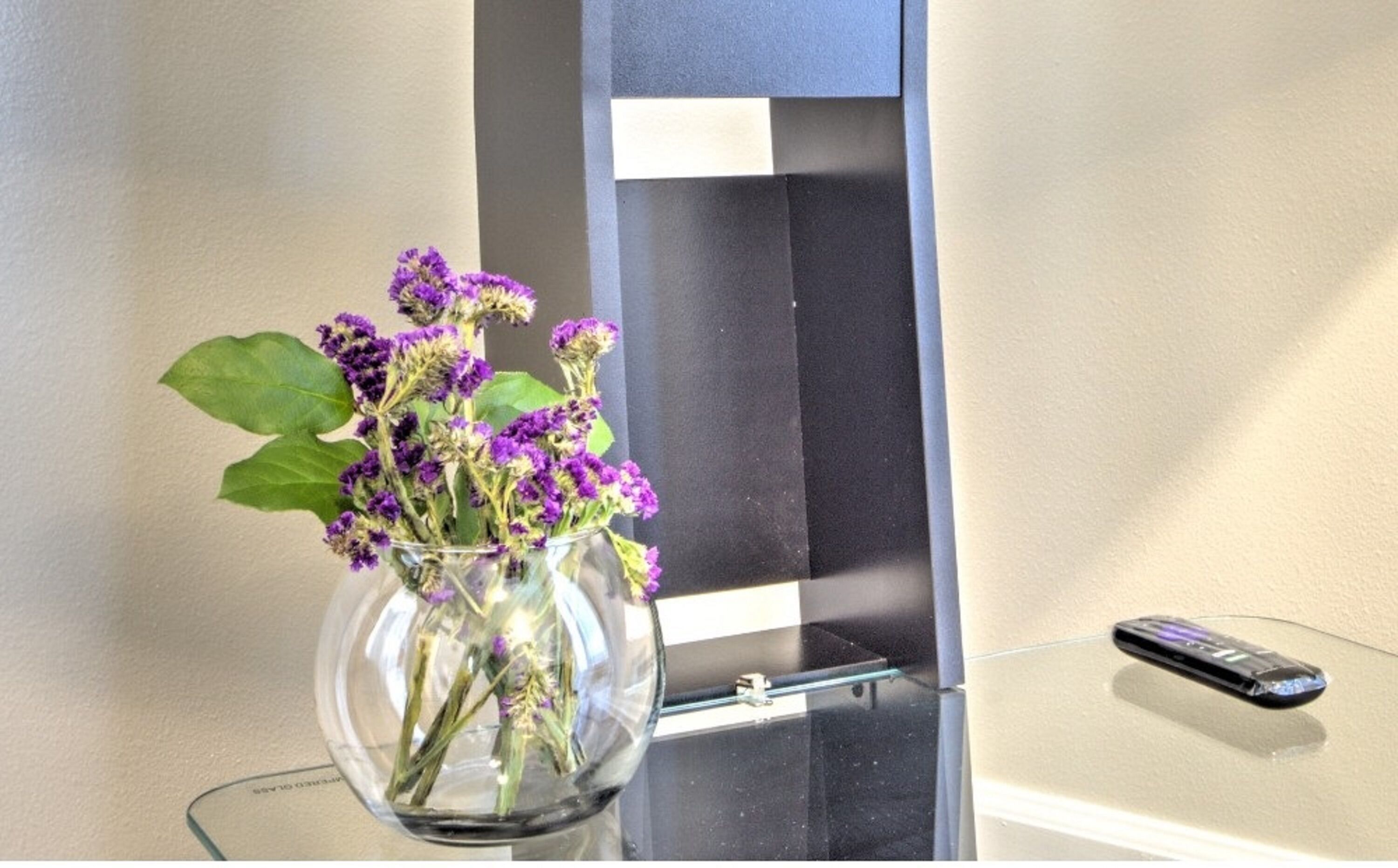 A clear glass vase with purple flowers on a reflective surface.