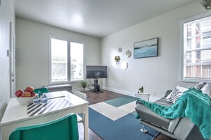 A modern living room with a flat-screen TV, a dining area with a table and chairs, and a sofa with a blanket.