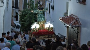 A narrow street with buildings on either side, a crowd of people, and a procession with a decorated carriage. - The countryside of Cruzchiquita (Alpandeire)