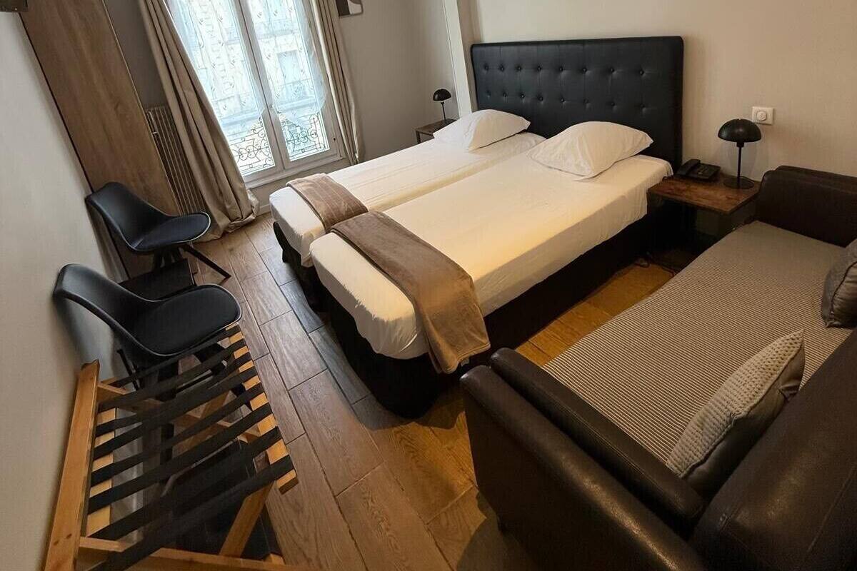 A hotel room with a large bed, a sofa, a desk with chairs, and a window with curtains.