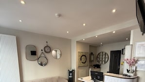 A modern living room with a sofa, a coffee table, and a dining area with a table and chairs. There are wall-mounted clocks and a mirror. - Lafayette Hotel (Paris)