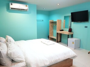 A hotel room with a bed, a TV, an air conditioner, a wooden shelf, and a small refrigerator.