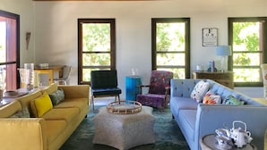 Una sala de estar acogedora con techo alto, vigas de madera y ventanas amplias. Hay dos sofás, una mesa de centro y un sillón.