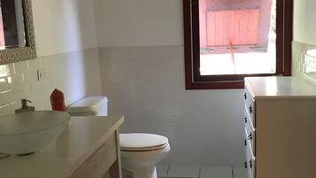 Een badkamer met een glazen wastafel, toilet, houten wastafelmeubel en een raam met houten kader.