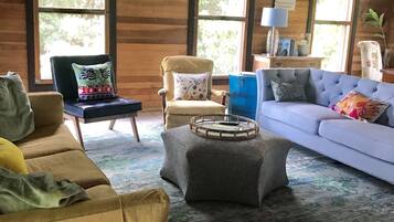 Una sala de estar acogedora con un sofá marrón, un sofá azul y un sillón con cojín. En el centro, una mesa redonda pequeña con una bandeja.