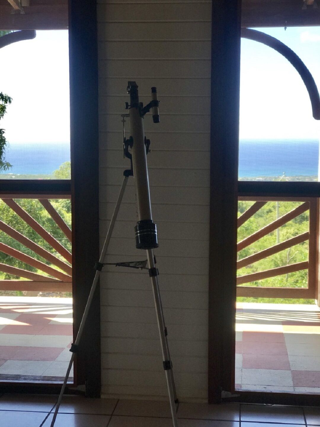Un telescopio su un treppiede all'interno di un edificio con vista sull'oceano.