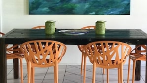Un comedor con una mesa de madera oscura, sillas naranjas y un cuadro abstracto grande en la pared.