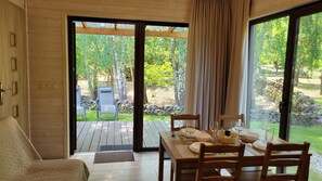 A wooden interior with a dining table set for four, a sofa, and a view of a garden through glass doors.