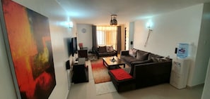 A living room with a sofa, coffee table, TV, and a water dispenser. - At Home With Ian (Ruaka)