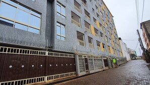 En byggnad med flera våningar, stora fönster och balkonger, med en inhägnad entré bestående av ett metallstaket och ett trästaket.