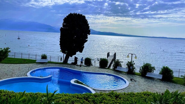 En swimmingpool med utsikt över havet och bergen i bakgrunden.