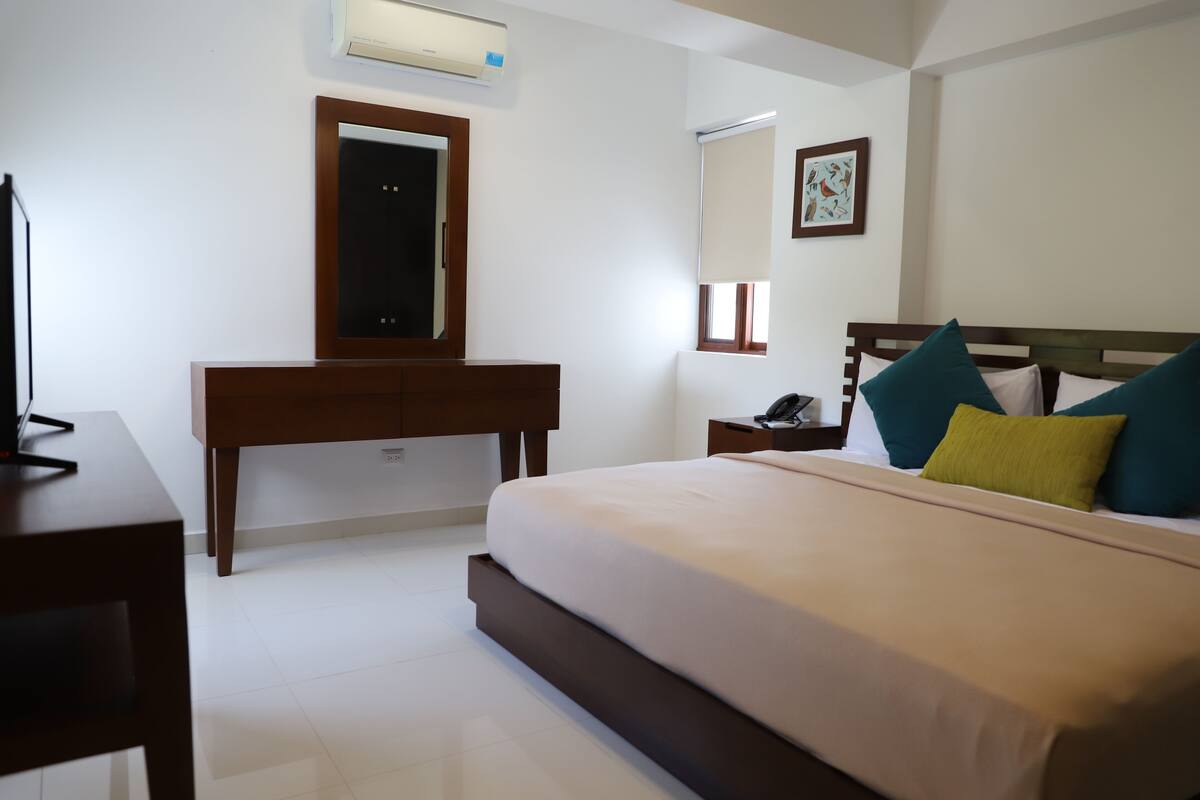 A bedroom with a bed, a desk, a mirror, a bedside table, and a wall-mounted air conditioner.