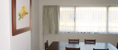 A dining area with a wooden table and chairs, a window with curtains, and a framed picture on the wall.