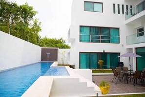 Un edificio moderno con piscina, zona de estar exterior y un jardín bien cuidado.