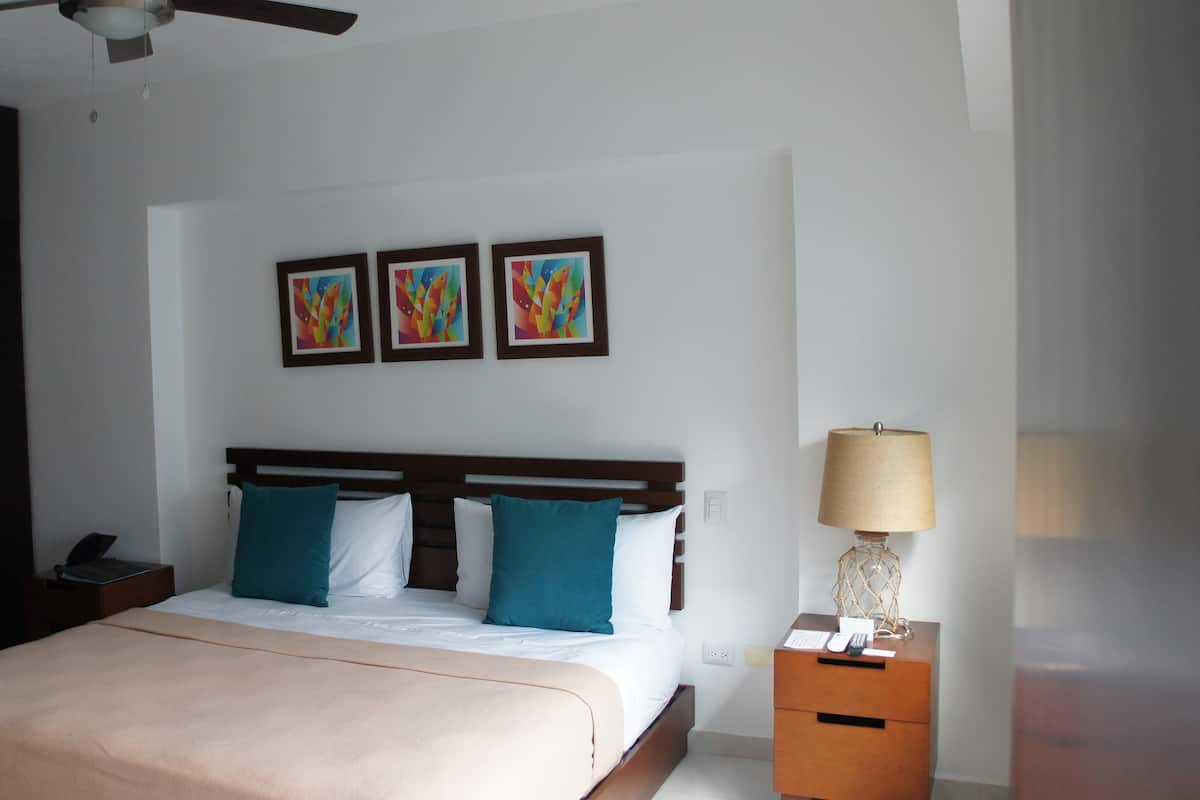 A hotel room with a bed, a nightstand, a lamp, and three abstract paintings on the wall.