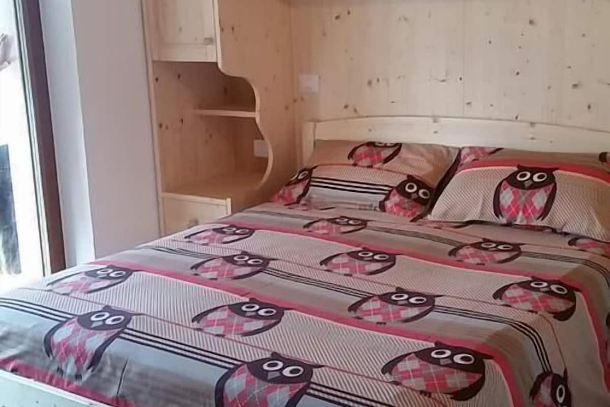A bedroom with a wooden bed frame, a patterned bedspread, and built-in wooden cabinets above the bed.