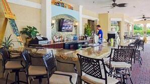 A bar area with a counter, bar stools, and a television screen. - Spacious and Lovely 3BD Unit With Balcony, Close to the Convention Center #3vc309 (Orlando)