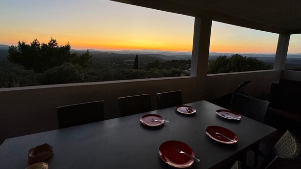 A dining table set with plates and cutlery, overlooking a scenic landscape during sunset.