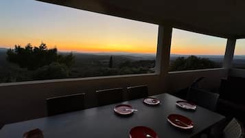 Mesa lista con platos y cubiertos, con vistas a un paisaje pintoresco al atardecer.