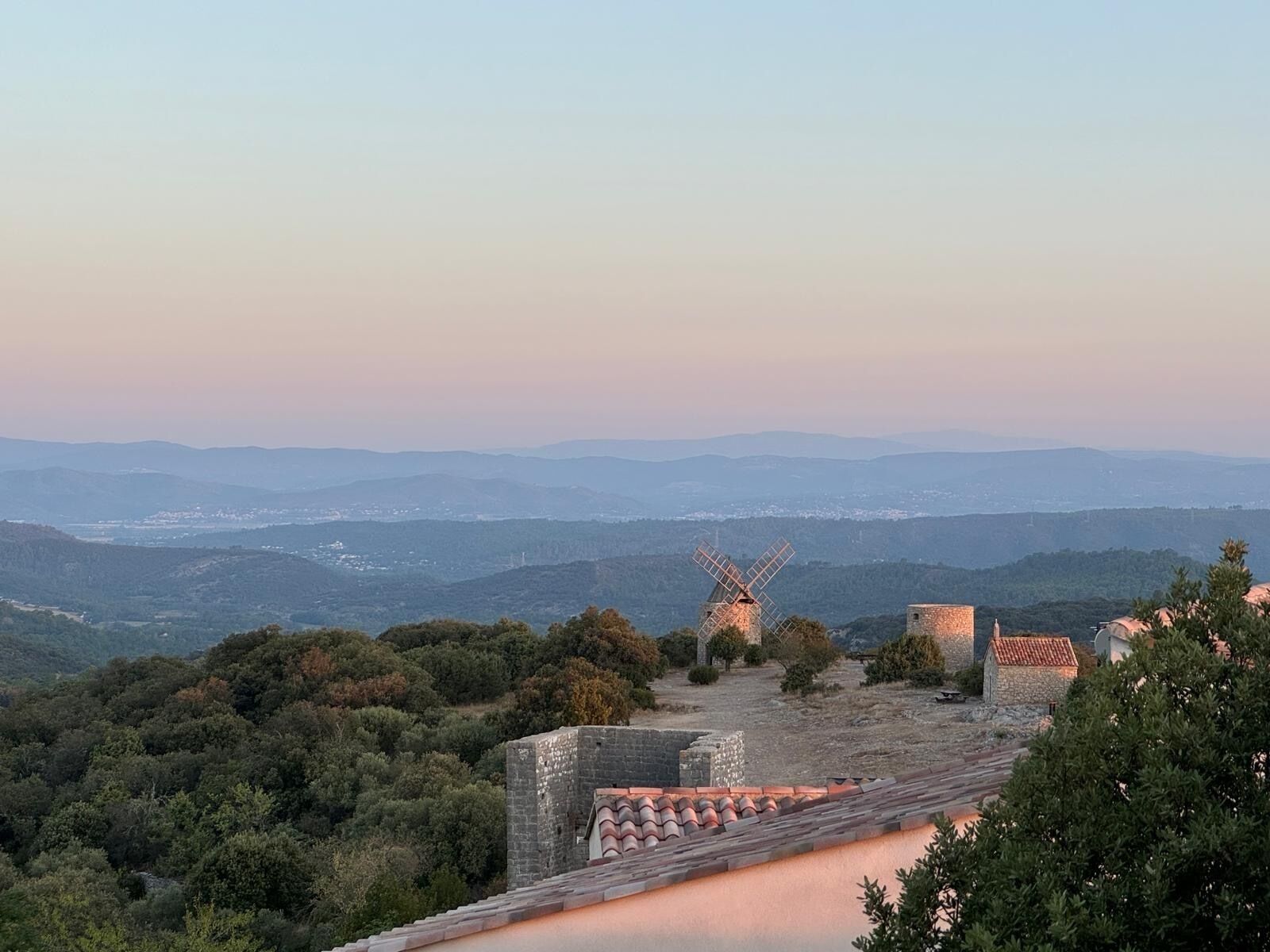 Un molino en una colina con vistas a montañas distantes y un edificio de piedra.