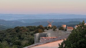 A windmill on a hill with a view of distant mountains and a stone building.