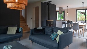 Una sala de estar moderna con un sofá, una mesa de centro y una chimenea. Se ve una escalera que sube a otro nivel.