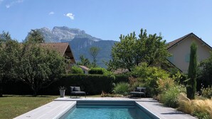 Una piscina rectangular con agua azul cristalina, rodeada por una terraza de madera y plantas en macetas.