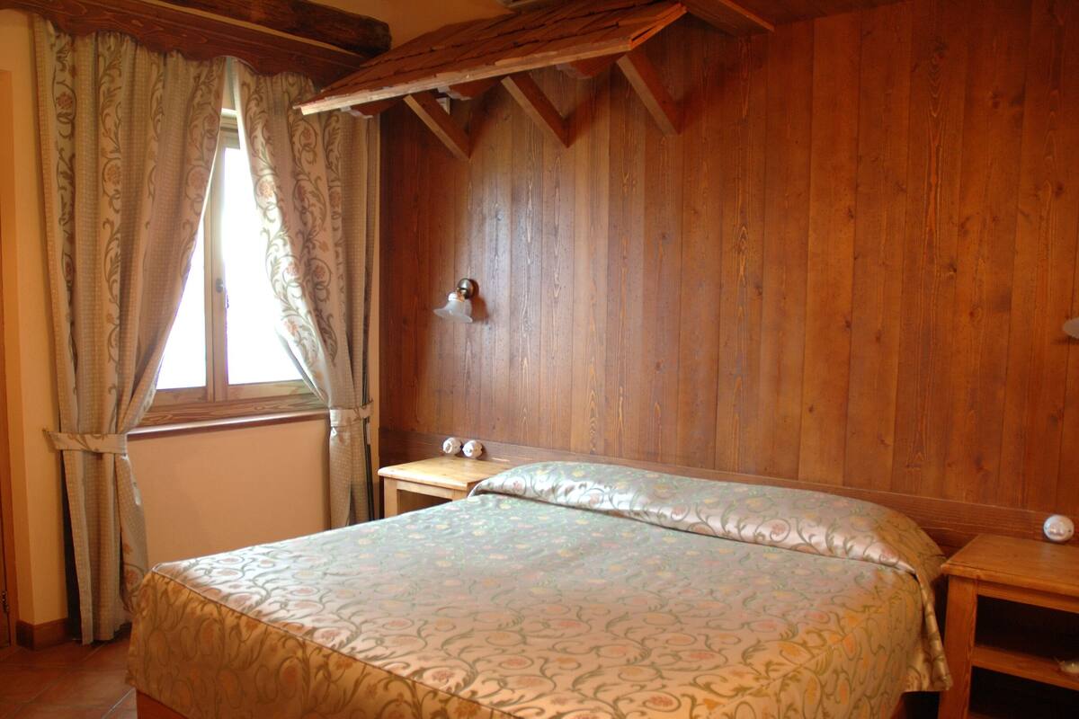 Una habitación de madera con una cama, una mesita de noche y una ventana con cortinas.