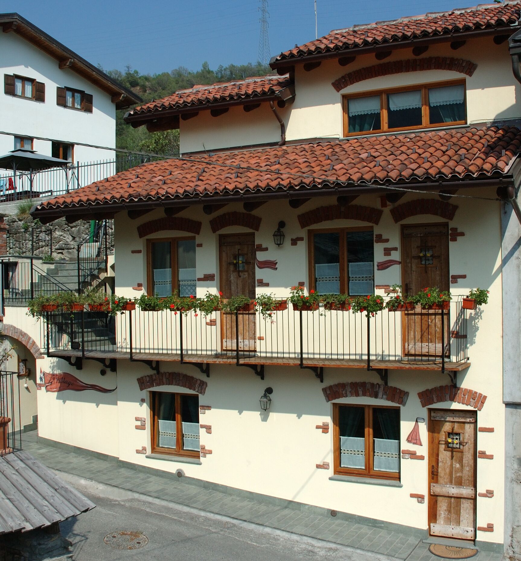 Un immeuble à plusieurs étages, de style architectural traditionnel, avec un toit en tuiles, des balcons en bois ornés de jardinières et un escalier en pierre.