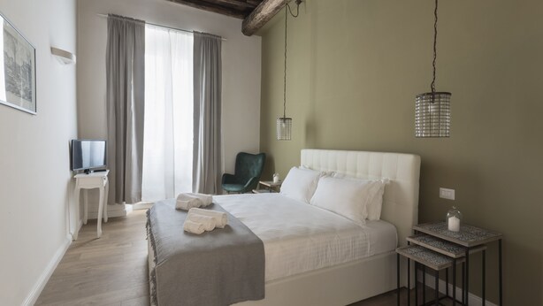 Une chambre avec un grand lit, un téléviseur posé sur une table de chevet, une chaise et un luminaire suspendu.