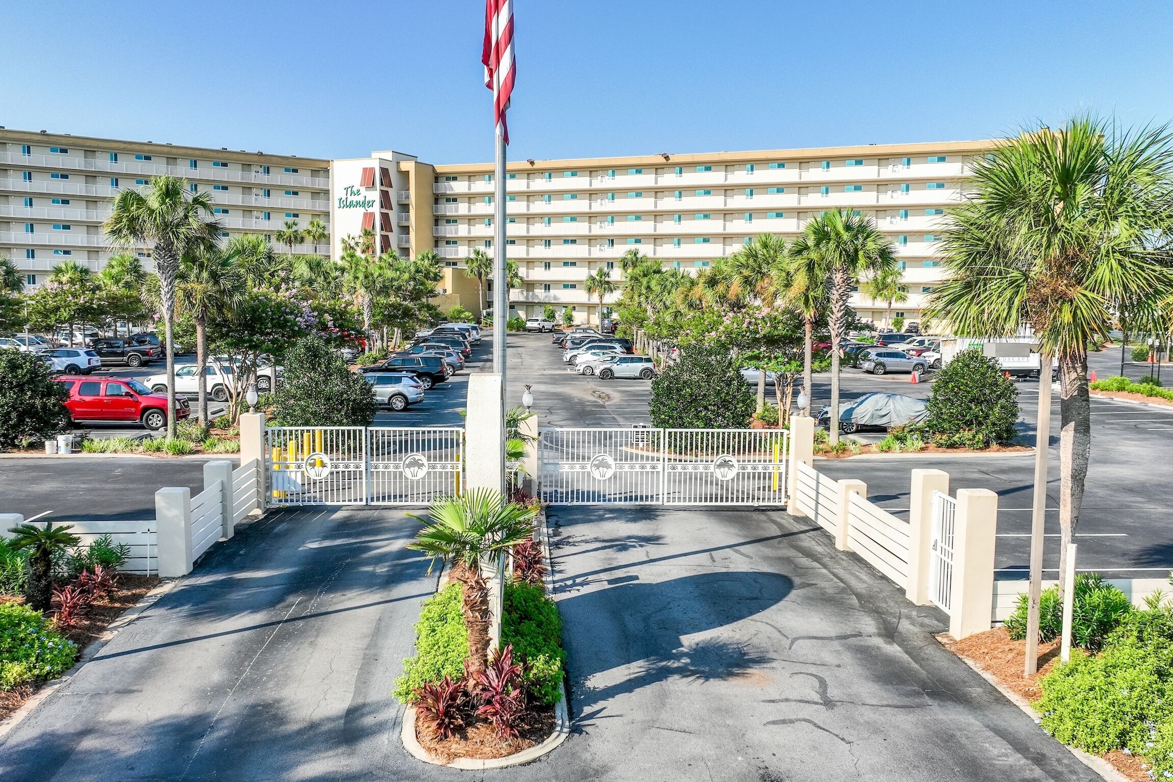 A hotel entrance with a gated driveway, palm trees, and a parking lot.