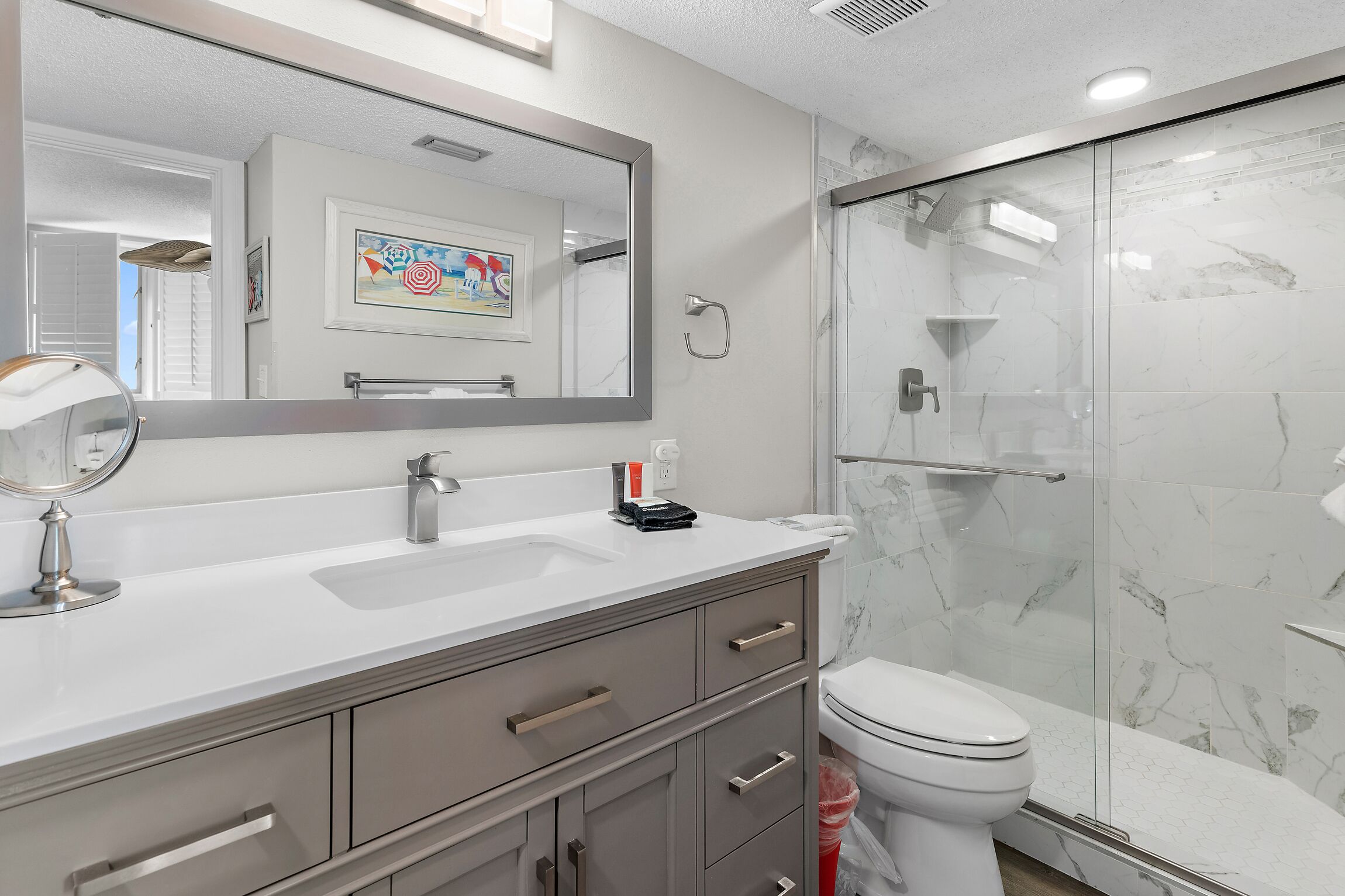 Uma casa de banho moderna com um espelho grande, uma sanita branca, loiça sanitária e um chuveiro com parede de vidro.