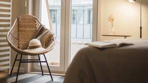 Una camera d'albergo con una sedia in vimini, un comodino con un vaso e una lampada.