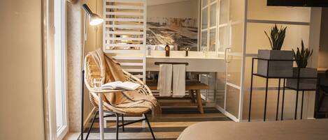 Una habitación de hotel moderna con una cama, una silla con un libro, un escritorio, un espejo y una planta en maceta.