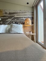 Quarto de hotel moderno com uma cama grande, luminária pendente e vista pela janela.