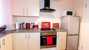 A modern kitchen with light wood cabinets, stainless steel appliances, a microwave, a red kettle, and a food-themed placemat. - Mycosy Lorimer 17 (Dundee)