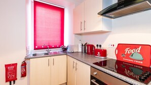 Une cuisine compacte avec un store rouge à la fenêtre, un évier en acier inoxydable, un grille-pain rouge et un extincteur rouge fixé au mur.
