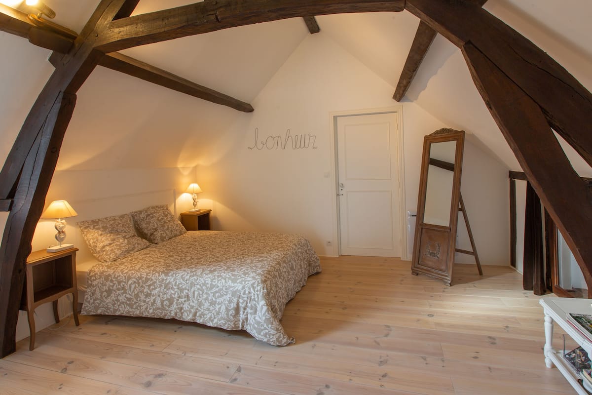 Un dormitorio con una cama, lámparas de noche, techo de madera, una puerta y un espejo.