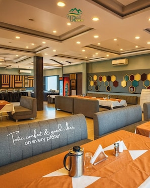 A hotel dining area with multiple seating options, including sofas and tables, and a wall with hexagonal patterns. - Virat Resorts, Sariska (Viratnagar)