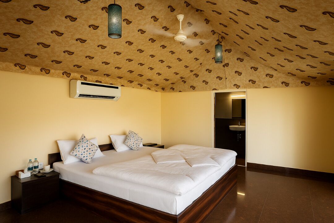 Habitación de hotel con una cama grande, un ventilador de techo, un equipo de aire acondicionado y un baño visible a través de una puerta abierta.