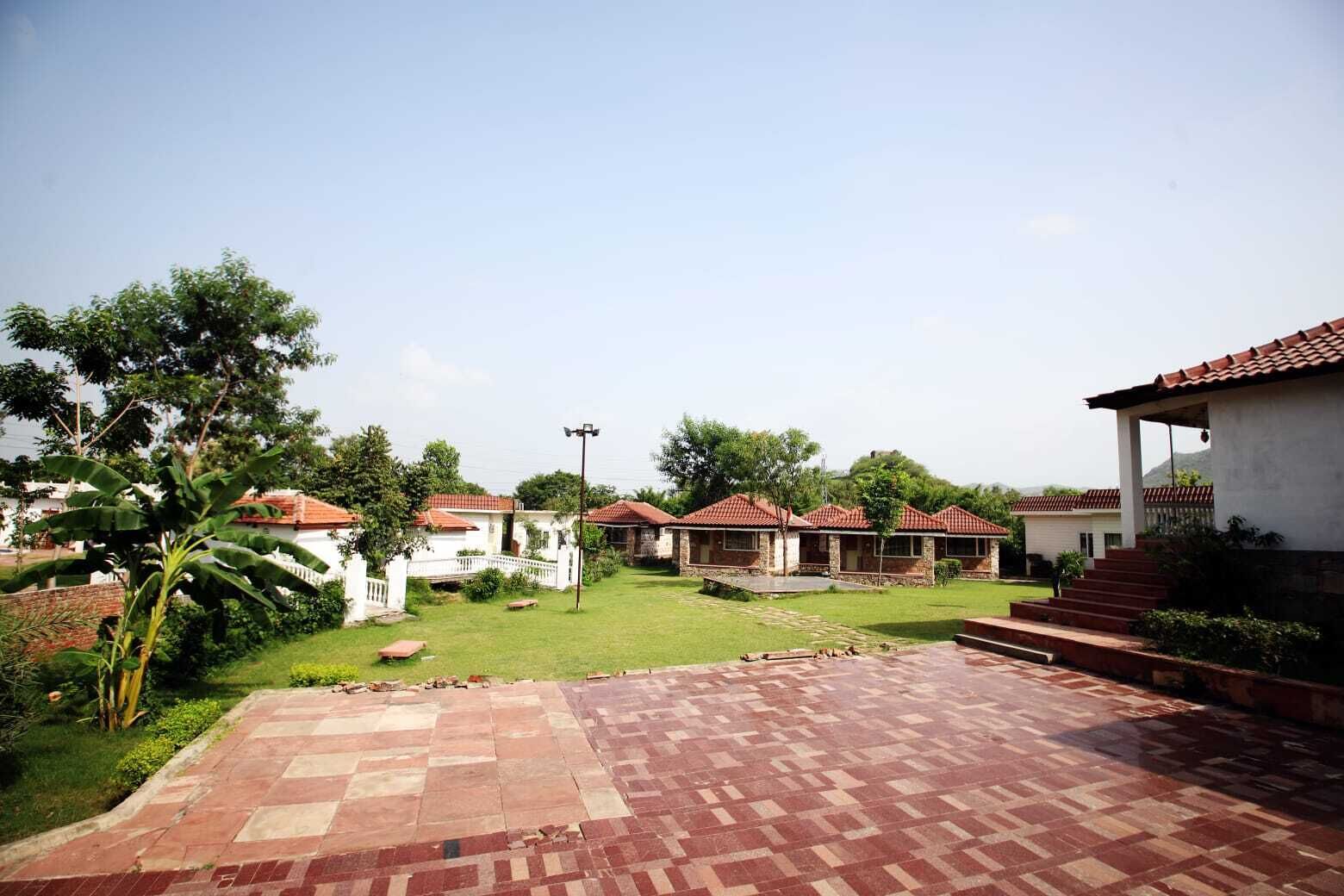 A courtyard with a paved walkway, several buildings with red-tiled roofs, and a grassy area with trees.