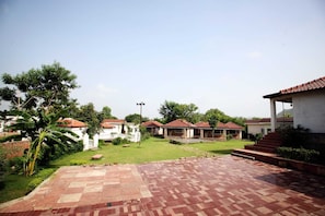 A courtyard with a paved walkway, several buildings with red-tiled roofs, and a grassy area with trees. - Virat Resorts, Sariska (Viratnagar)