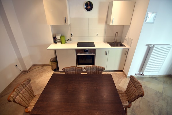 A modern kitchen with white cabinets, a built-in oven, and a dining area with a wooden table and patterned chairs.