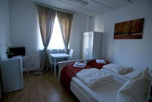 A hotel room with a bed, a desk, a chair, a wardrobe, and a television.