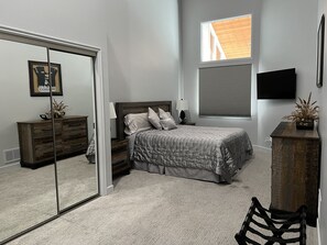 A bedroom with a bed, a dresser, a mirror, a window with blinds, and a television on the wall. - Park City in the summer. Stay in completely remodeled condo close to Main Street (Park City)