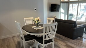 A dining area with a round table, white chairs, and a vase of flowers. There is a dark-colored sofa and a TV mounted on the wall. - Park City in the summer. Stay in completely remodeled condo close to Main Street (Park City)