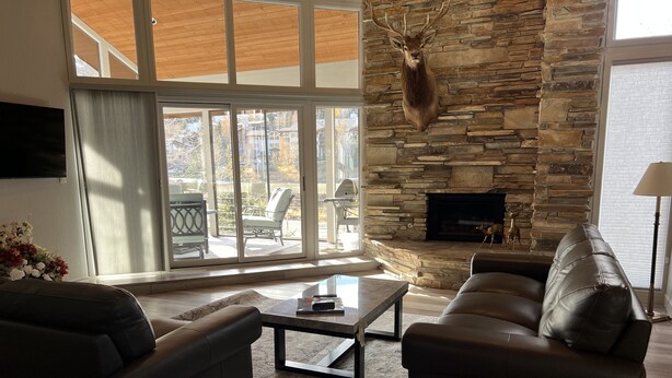 A living room with a stone fireplace, leather sofas, and a large window overlooking a patio area. - Park City in the summer. Stay in completely remodeled condo close to Main Street (Park City)